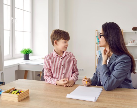 A boy sitting at a table opposite a clinician during an assessment session