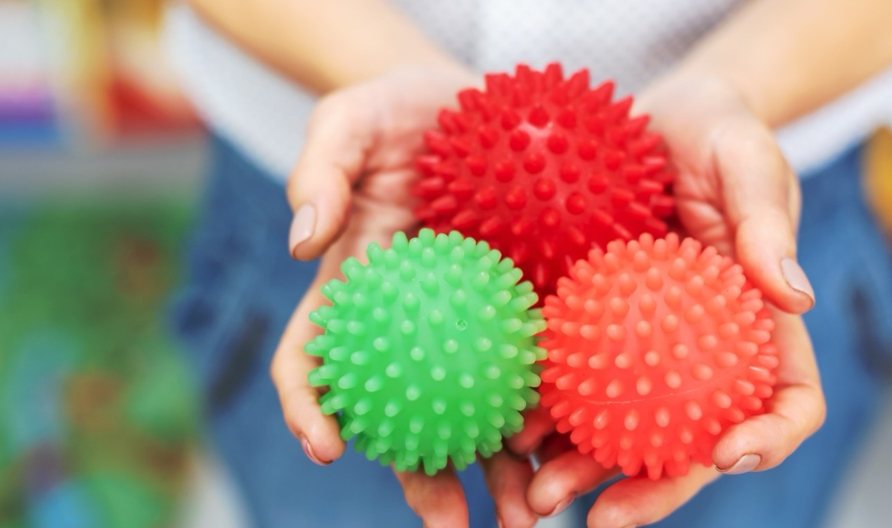 A pair of hands holding three textured sensory balls
