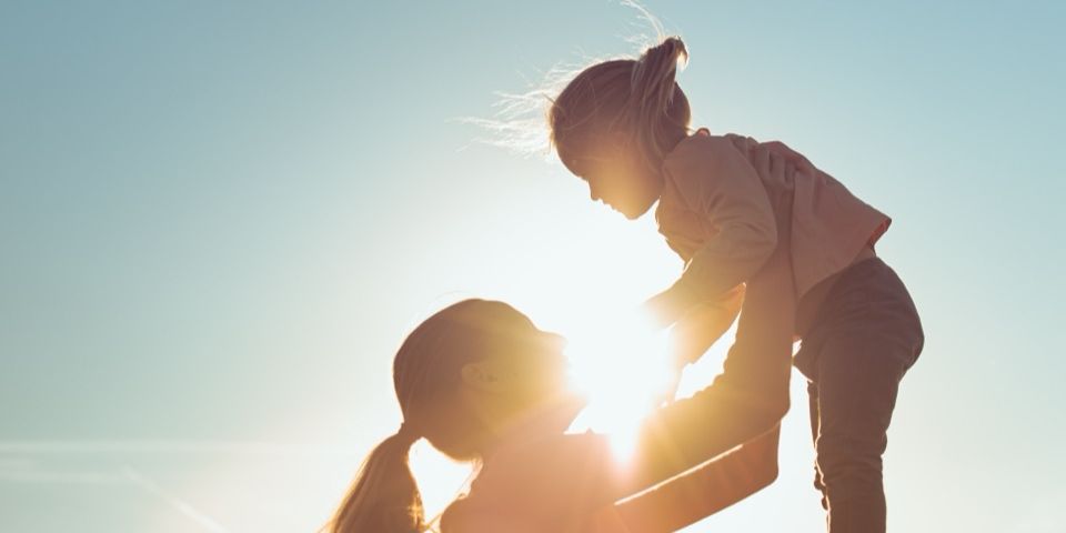A parent lifting a laughing child into the air in a field at sunset