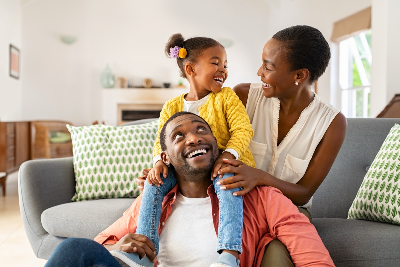 A mother, father and young daughter laughing together on a sofa at home.